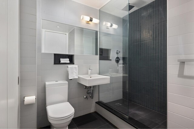 bathroom featuring sink, tile walls, tiled shower, toilet, and tile patterned floors