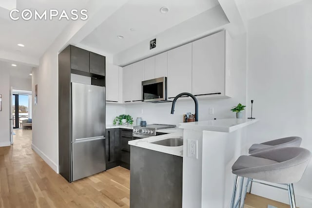 kitchen with modern cabinets, light wood-style flooring, stainless steel appliances, a breakfast bar area, and light countertops