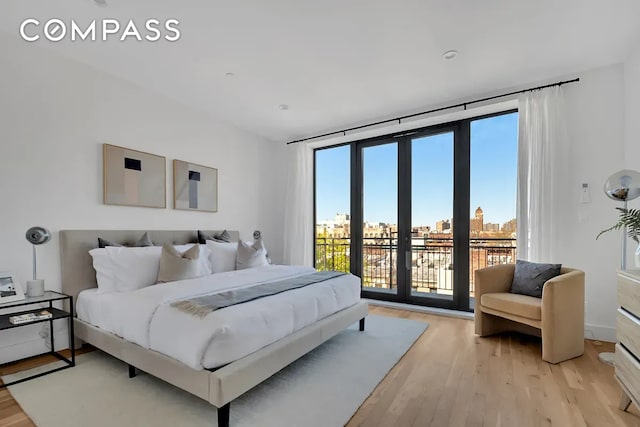 bedroom featuring access to exterior, a city view, light wood finished floors, and a wall of windows