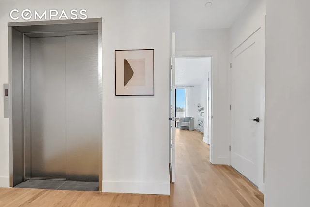 hallway with elevator and light wood finished floors