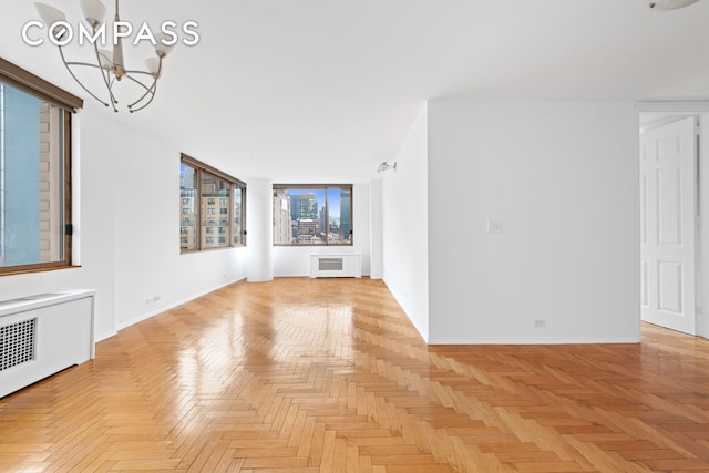 unfurnished living room featuring radiator heating unit, baseboards, and a chandelier