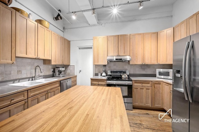 kitchen with stainless steel appliances, tasteful backsplash, light brown cabinets, a sink, and under cabinet range hood