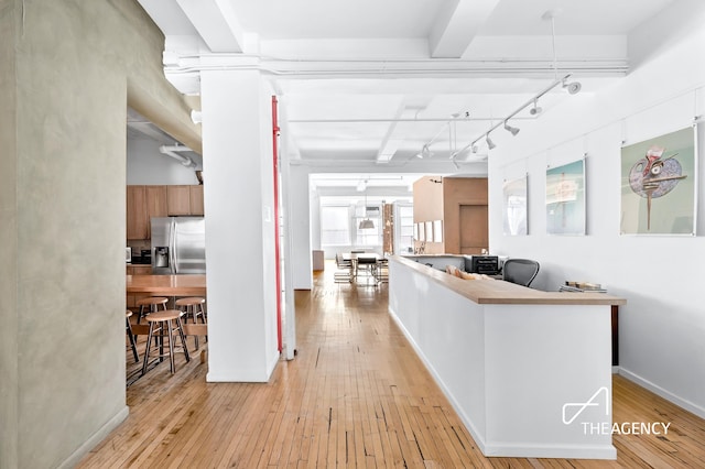 corridor featuring light wood finished floors, beamed ceiling, rail lighting, and baseboards