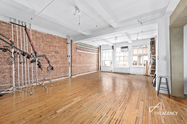 exercise room with radiator, brick wall, and wood-type flooring
