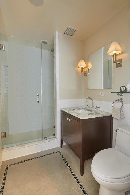 bathroom featuring toilet, vanity, tile patterned flooring, and a shower with door