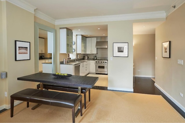 kitchen with stainless steel appliances, crown molding, white cabinets, and wall chimney range hood