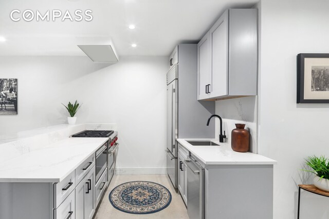 kitchen featuring gray cabinets, high end appliances, sink, and light stone counters