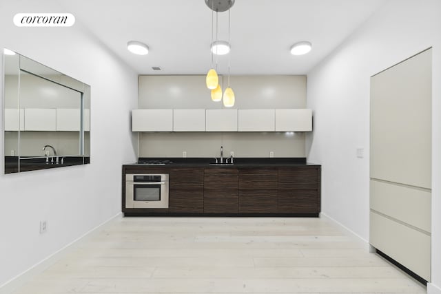 kitchen with white cabinetry, stainless steel oven, dark brown cabinets, pendant lighting, and sink