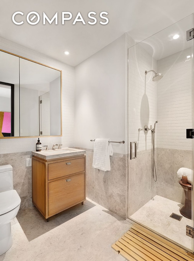 bathroom featuring tile walls, toilet, a stall shower, wainscoting, and vanity