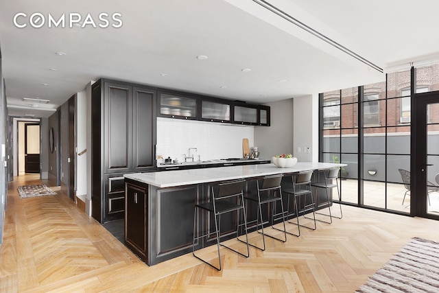 kitchen with a spacious island, glass insert cabinets, a breakfast bar, light countertops, and backsplash