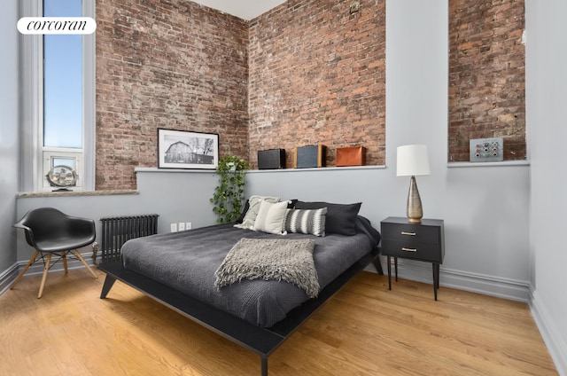 bedroom featuring radiator, light hardwood / wood-style floors, and brick wall