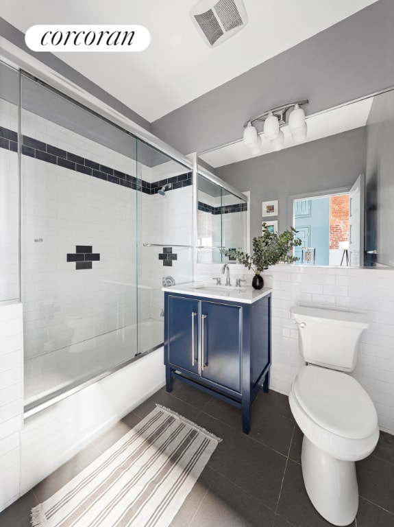 full bathroom with tile patterned floors, toilet, combined bath / shower with glass door, tile walls, and vanity