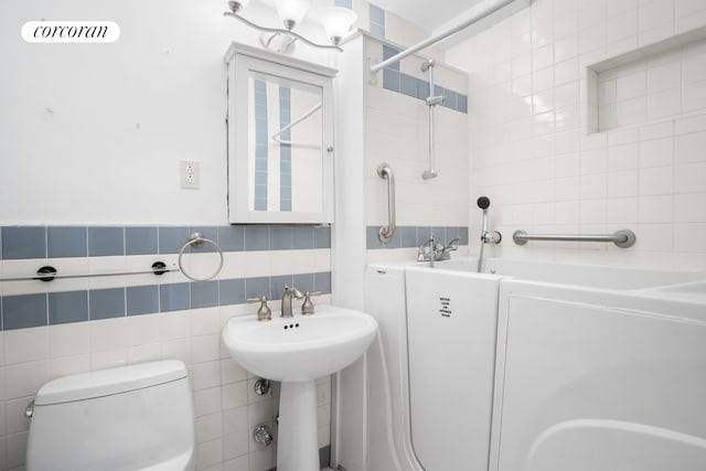 bathroom with washer / clothes dryer, a sink, walk in shower, toilet, and tile walls