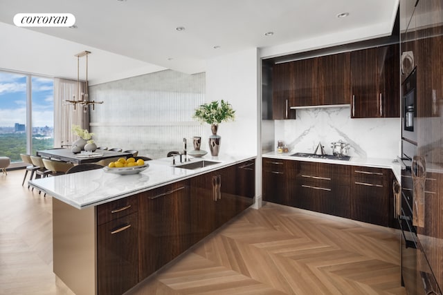 kitchen featuring light stone countertops, decorative light fixtures, sink, stainless steel gas cooktop, and light parquet floors