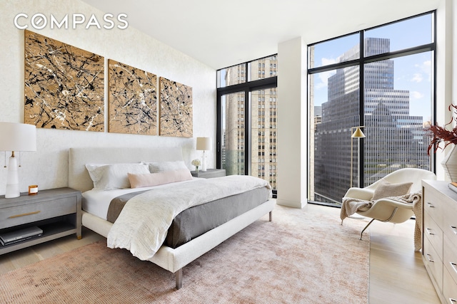 bedroom featuring light wood-type flooring, access to exterior, a wall of windows, and a city view