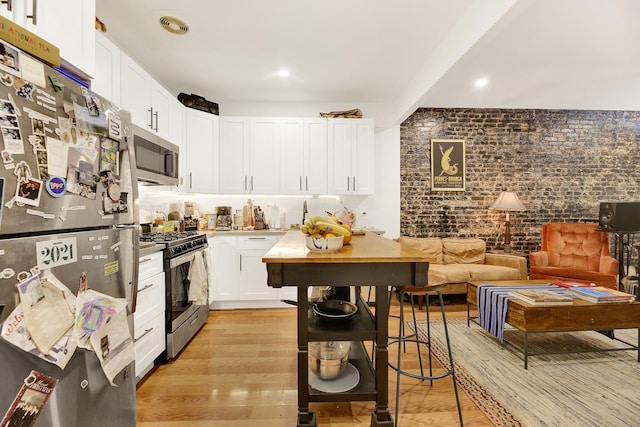 kitchen with visible vents, brick wall, light wood-style flooring, appliances with stainless steel finishes, and white cabinetry