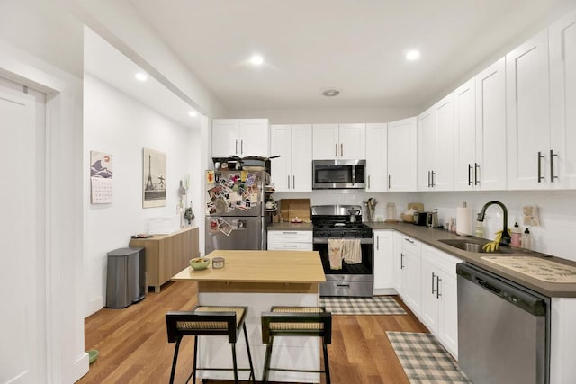 kitchen with sink, wood-type flooring, appliances with stainless steel finishes, a kitchen island, and white cabinets