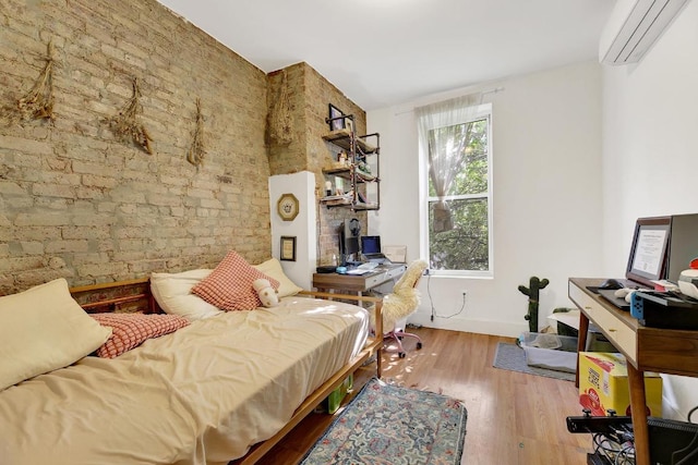 bedroom with light hardwood / wood-style floors, an AC wall unit, and brick wall