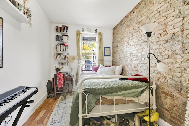 bedroom featuring brick wall, baseboards, and wood finished floors