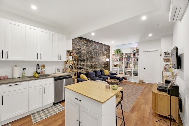 kitchen with light wood finished floors, a sink, a wall mounted air conditioner, stainless steel dishwasher, and open floor plan