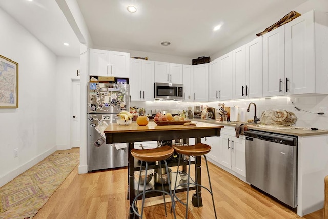 kitchen featuring white cabinetry, appliances with stainless steel finishes, decorative backsplash, and light wood-type flooring