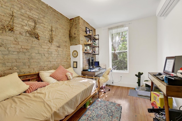 bedroom with a wall unit AC, wood finished floors, and brick wall