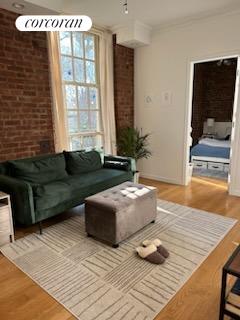 living room with crown molding, hardwood / wood-style flooring, and brick wall