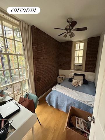 bedroom featuring ceiling fan, brick wall, and wood-type flooring