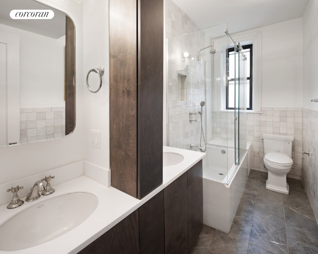 full bathroom featuring toilet, combined bath / shower with glass door, tile walls, and vanity