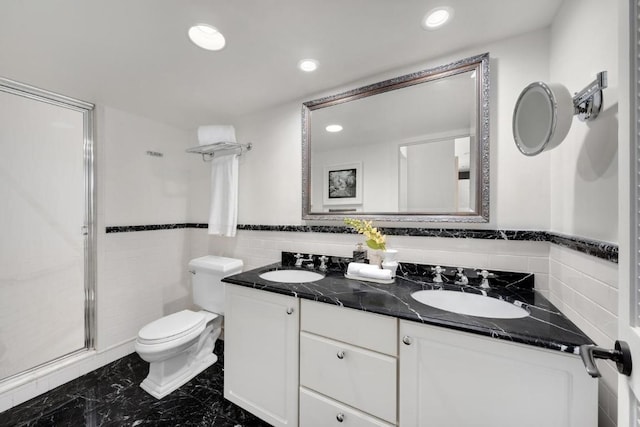 bathroom with vanity, toilet, a shower with door, and tile walls