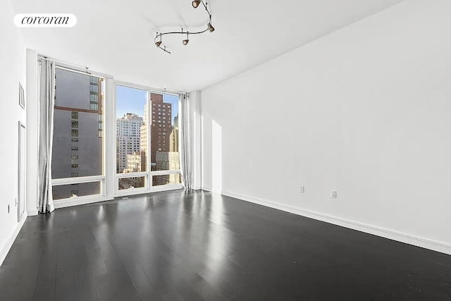 spare room featuring a view of city, dark wood-style flooring, floor to ceiling windows, visible vents, and baseboards