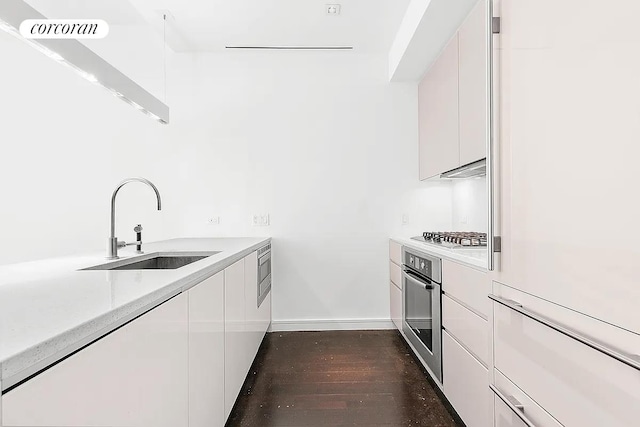 kitchen with dark wood finished floors, stainless steel appliances, light countertops, white cabinetry, and a sink