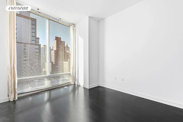 empty room with a city view, dark wood-style flooring, and baseboards