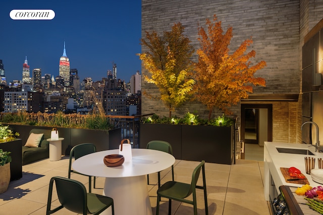 patio at night featuring a sink, outdoor dining space, and a view of city lights