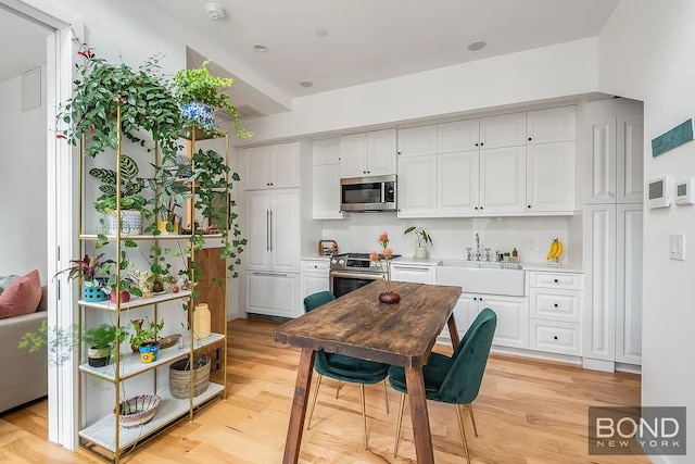 kitchen with stainless steel appliances, a sink, white cabinetry, and light wood-style floors