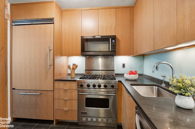 kitchen with stainless steel appliances, dark tile patterned flooring, dark countertops, and a sink