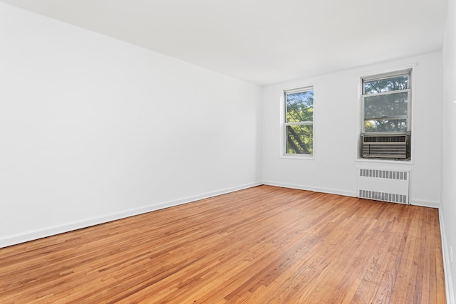 spare room featuring radiator, light wood finished floors, and baseboards