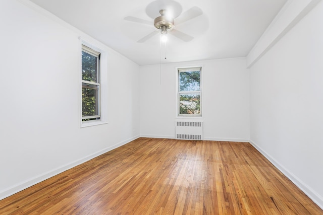 unfurnished room featuring radiator, light wood-type flooring, baseboards, and a ceiling fan