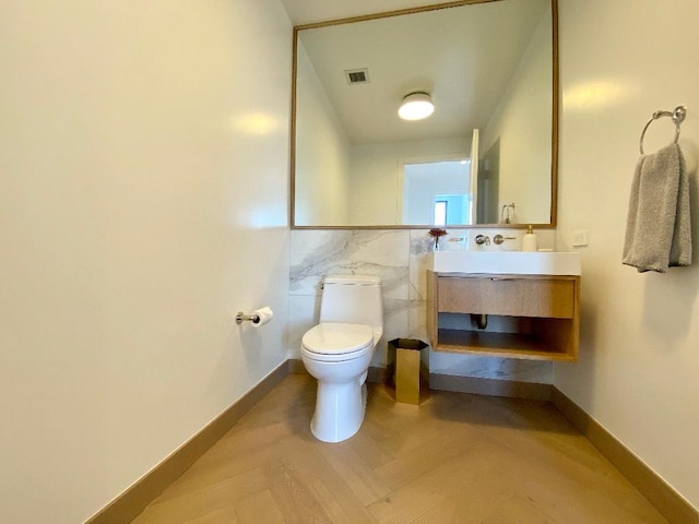 half bath with tile walls, visible vents, toilet, vanity, and baseboards