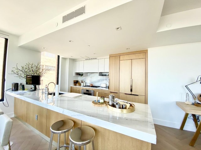 kitchen with visible vents, light stone countertops, light brown cabinets, white cabinetry, and a sink