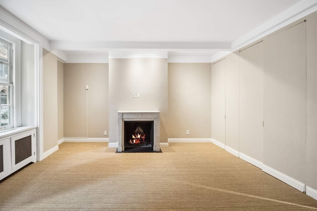 unfurnished living room featuring a fireplace with flush hearth, light colored carpet, and baseboards