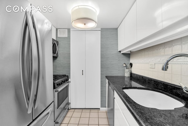 kitchen with light tile patterned floors, stainless steel appliances, white cabinets, a sink, and dark stone counters