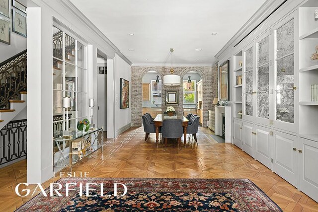 dining space with light parquet floors, ornamental molding, and brick wall