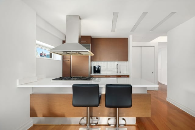 kitchen featuring sink, kitchen peninsula, island exhaust hood, and a breakfast bar area