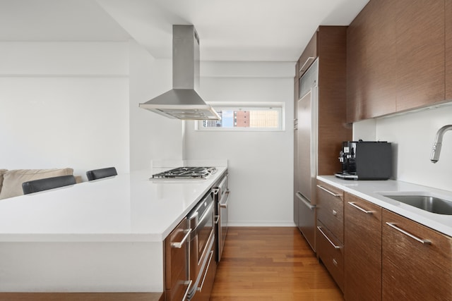 kitchen with stainless steel gas stovetop, light hardwood / wood-style floors, a kitchen bar, sink, and island range hood