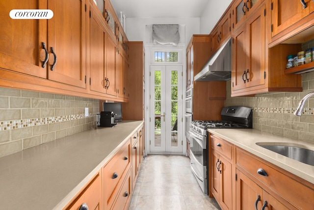 kitchen with under cabinet range hood, stainless steel range with gas cooktop, brown cabinetry, and a sink