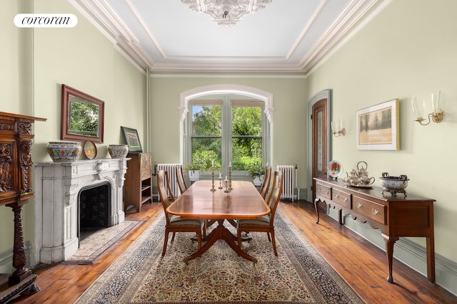 dining room with ornamental molding, wood-type flooring, a fireplace, and radiator heating unit