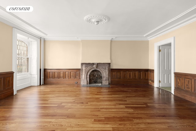 unfurnished living room featuring visible vents, a wainscoted wall, a fireplace with flush hearth, wood finished floors, and crown molding