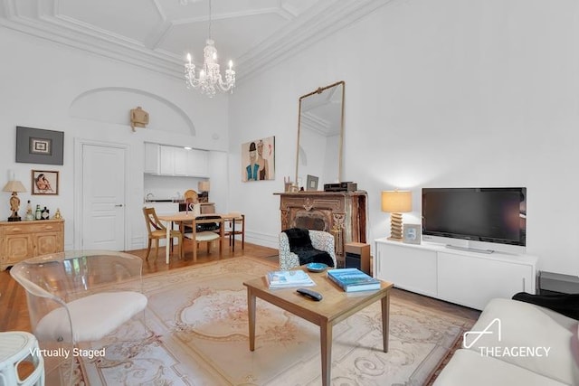 living room featuring a towering ceiling, a chandelier, ornamental molding, coffered ceiling, and light hardwood / wood-style floors