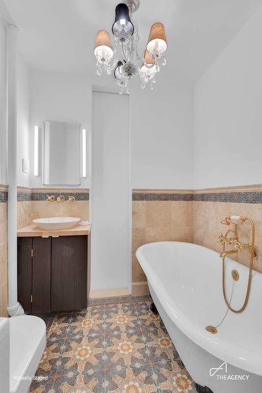 1388 Lexington Ave Unit 2W, New York City, NY 10128 - bathroom featuring a freestanding bath, vanity, tile walls, a wainscoted wall, and a chandelier